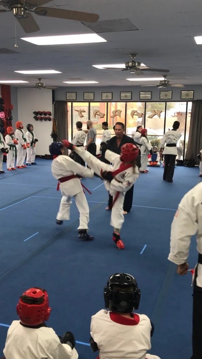 Students sparring in dojo with instructor supervising